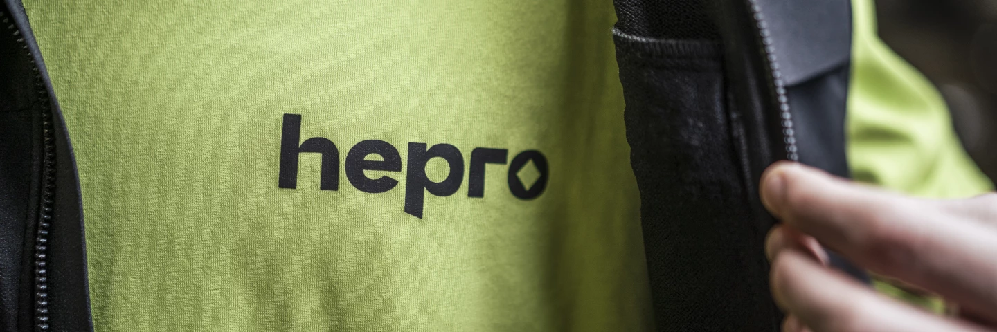 Nahaufnahme eines Mitarbeiters in einem grünen Shirt mit dem hepro-Logo auf der Brust und einer schwarzen Weste mit dem hepro-Logo auf der Schulter.