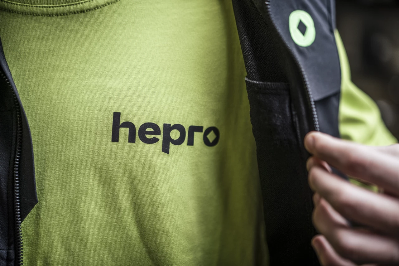 Nahaufnahme eines Mitarbeiters in einem grünen Shirt mit dem hepro-Logo auf der Brust und einer schwarzen Weste mit dem hepro-Logo auf der Schulter.