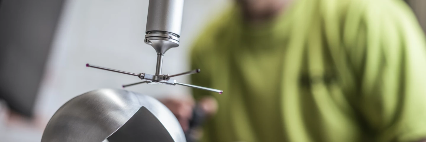 Mitarbeiter bei der Qualitätsprüfung eines metallischen Bauteils, das eine quadratische Vertiefung aufweist, mit einem Präzisionsmessgerät, das über das Werkstück gehalten wird.